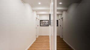 A hallway with white walls and wooden flooring, leading to a room with a framed picture on the wall. - GuestReady - Uptown suites 3 (Porto)