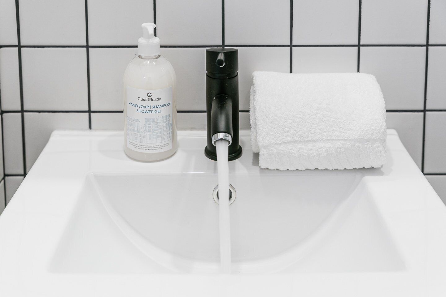 Un lavabo de salle de bain avec un flacon de savon liquide, un robinet noir et une serviette blanche.