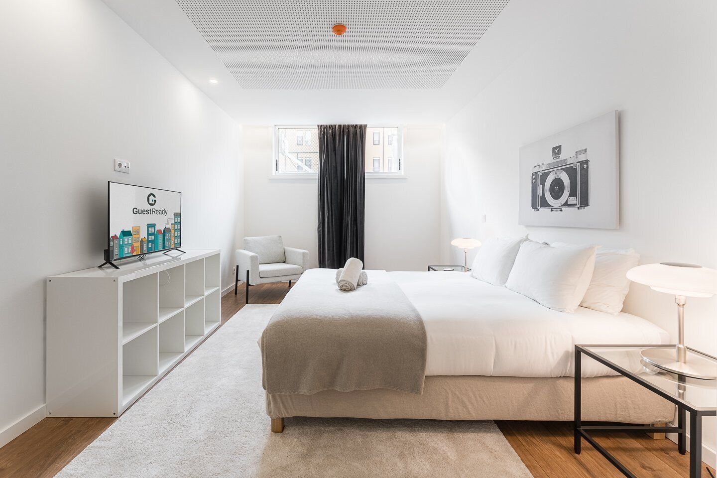 Una habitación de hotel moderna con una cama grande, un escritorio, una silla, un televisor y una ventana con cortinas.