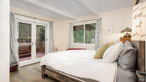 A bedroom with a large bed, a sliding glass door to a balcony, and a view of greenery outside.