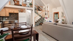 A spacious living area with a high ceiling, a staircase leading to an upper level, and a kitchen with wooden cabinets and a tiled backsplash.