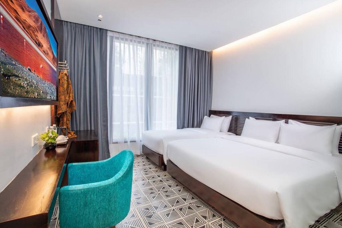 Habitación de hotel con una cama grande, dos mesitas de noche, un escritorio con silla y un ventanal con cortinas.