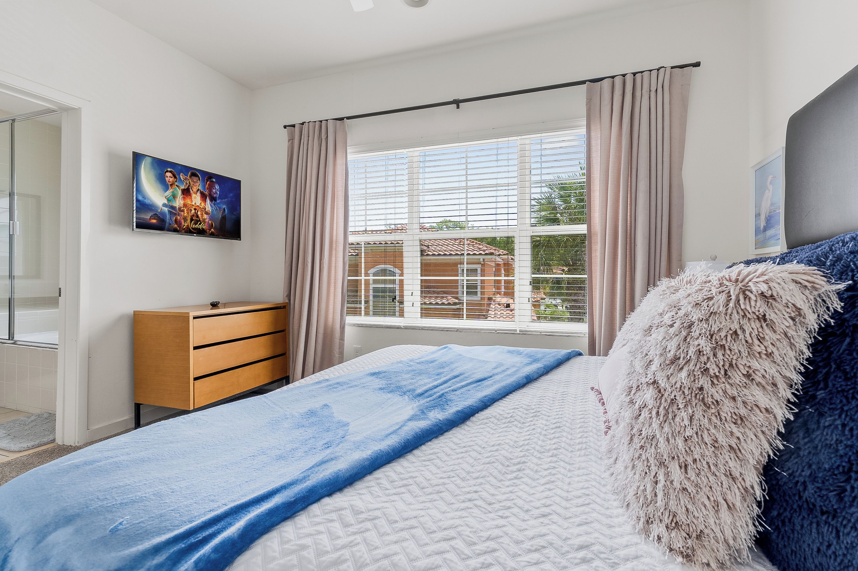 Una camera da letto con un letto, una cassettiera in legno, una finestra con tende e un quadro appeso al muro.