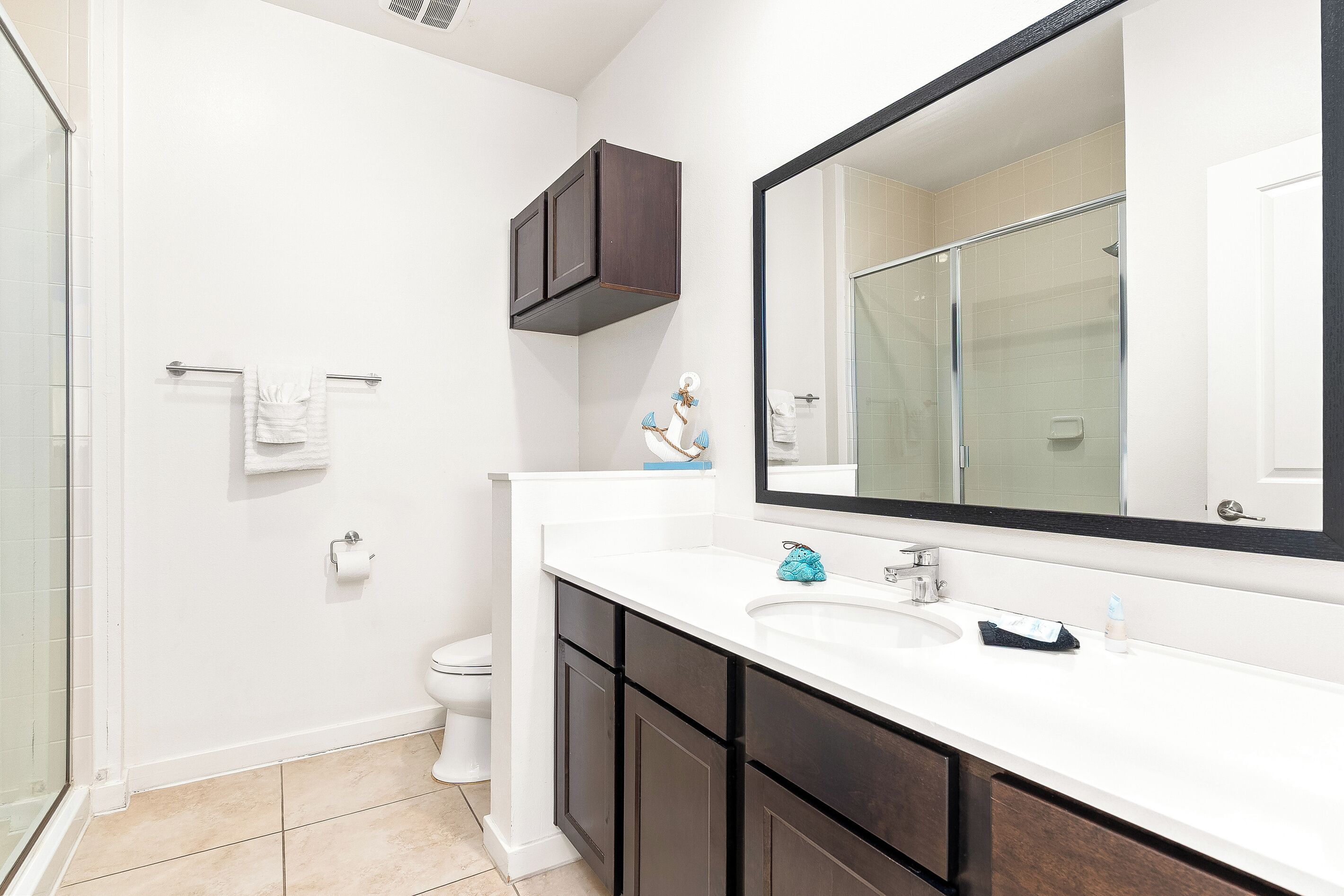 Une salle de bain avec un lavabo blanc, des meubles sombres, un grand miroir et une cabine de douche en verre.