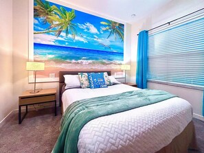 Quarto com mural de tema praiano, uma cama com manta verde, duas luminárias de cabeceira e uma janela com cortinas azuis.