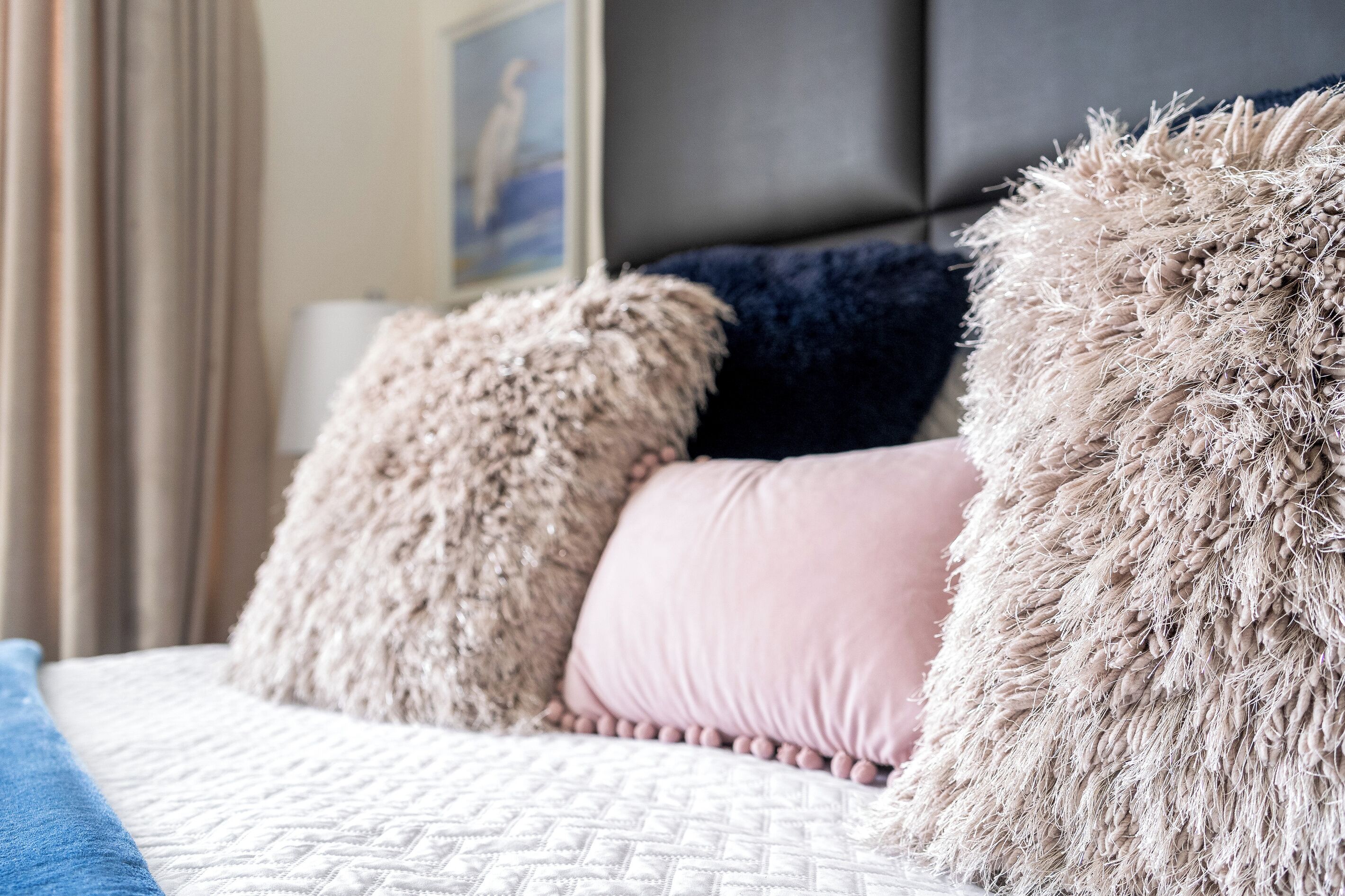 A bed with a textured white cover, two fluffy pillows, and a dark headboard.