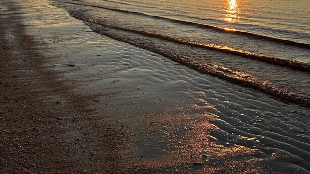 A beach at sunset with waves gently lapping onto the shore.
