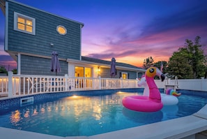 Una piscina con juguetes inflables, una casa con terraza y un cielo al atardecer.