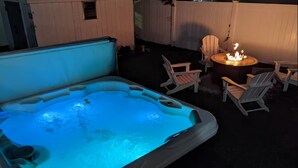 A hot tub with a fire feature, surrounded by Adirondack chairs, in an outdoor setting.