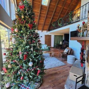 A spacious living room with a large Christmas tree, wooden flooring, and a stone fireplace.
