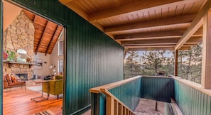 A cozy interior with a stone fireplace, a wooden ceiling, and a view of trees outside.