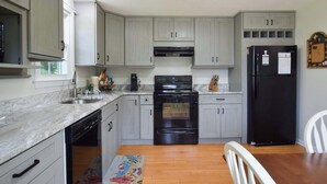 Una cocina con armarios grises claros, una estufa negra, un refrigerador negro y una mesa de comedor de madera con una silla blanca.