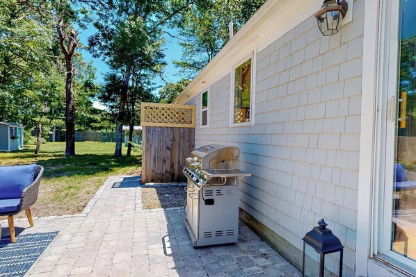 A patio area with a grill, a chair, and a wooden fence.