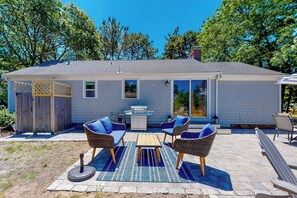 Een huis met een patio, rieten meubilair en een barbecue.