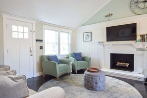 A living room with two green armchairs, a grey ottoman, a fireplace, and a mounted television.