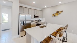 Una cocina moderna con electrodomésticos de acero inoxidable, una isla blanca con taburetes y un elemento decorativo en la pared.