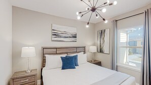 Un dormitorio ordenado con una cama grande, mesitas de noche con lámparas, una lámpara de techo moderna y obras de arte en las paredes.