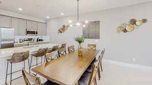 Una cocina moderna con electrodomésticos de acero inoxidable, una mesa de comedor de madera y una araña.