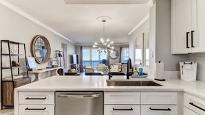 Une cuisine moderne avec des meubles blancs, un îlot central doté d’un évier et une grande fenêtre offrant une vue sur l’extérieur.