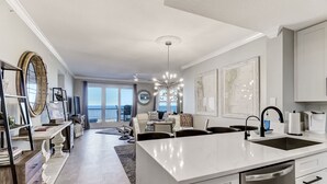 Une cuisine moderne dotée d’un grand îlot central, de meubles blancs et offrant une vue sur l’espace de vie.