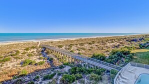 Une vue sur la côte, avec une jetée en bois menant à une plage, un espace piscine et un ciel dégagé.