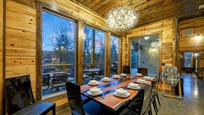 A wooden interior with a dining area, large windows, and a chandelier. - Charming Creekside Escape: Pool, Putt-Putt, Game Room & Pet Friendly (Broken Bow)