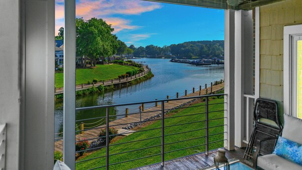 A balcony with a view of a river, a wooden deck, and a grassy area.