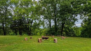 A grassy field with several wooden stumps and a fire pit. - Taneycomo Waterfront Retreat with Private Indoor Pool, Hot Tub, Game Room & $400 Daily Tickets (Branson)