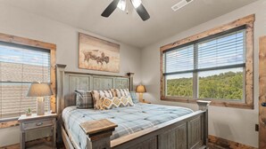 A bedroom with a large bed, two bedside tables, a ceiling fan, and a window with blinds. - Taneycomo Waterfront Retreat with Private Indoor Pool, Hot Tub, Game Room & $400 Daily Tickets (Branson)