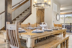 A dining area with a wooden table set for six, a staircase, and a chandelier.