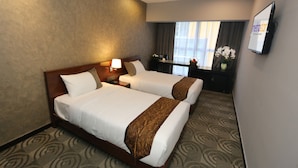 Une chambre d’hôtel avec deux lits, une télévision, un bureau et une fenêtre avec des rideaux.