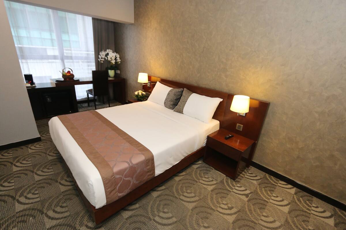 Een hotelkamer met een groot bed, twee bedlampen, een bureau met stoel, en een raam met gordijnen.