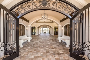 A spacious hallway with a tiled floor, white benches, and ornate black metal railings.