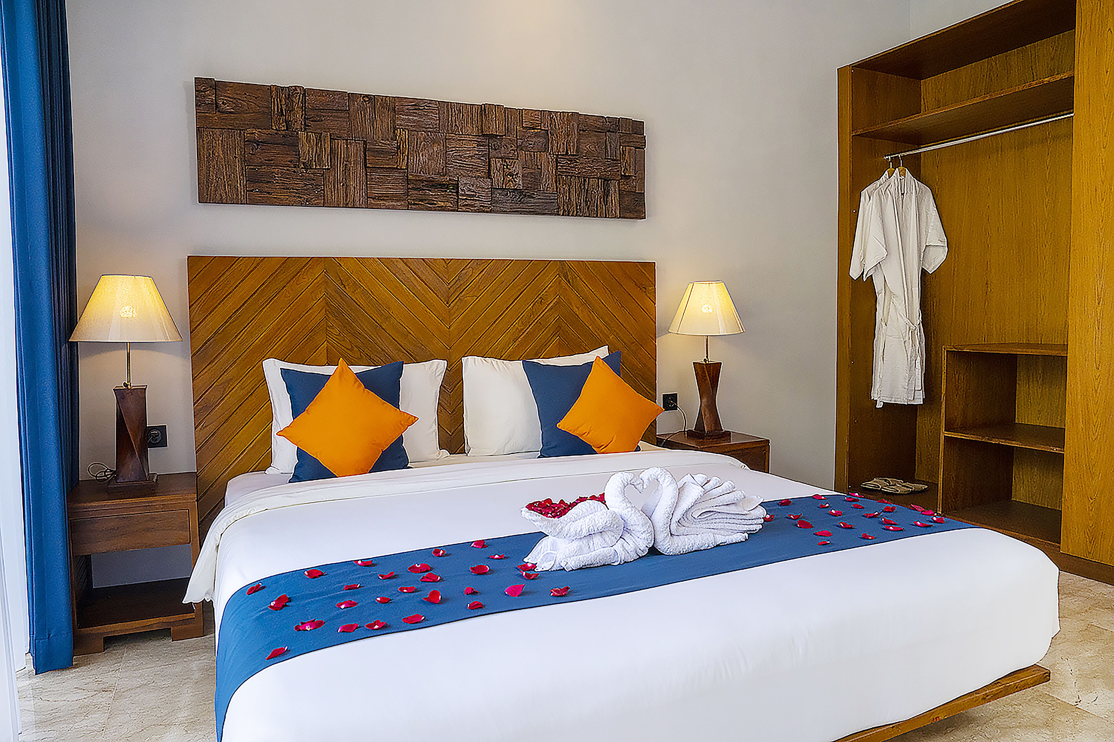 Una cama bien hecha con una colcha azul y blanca, dos lámparas a cada lado y un cabecero de madera.