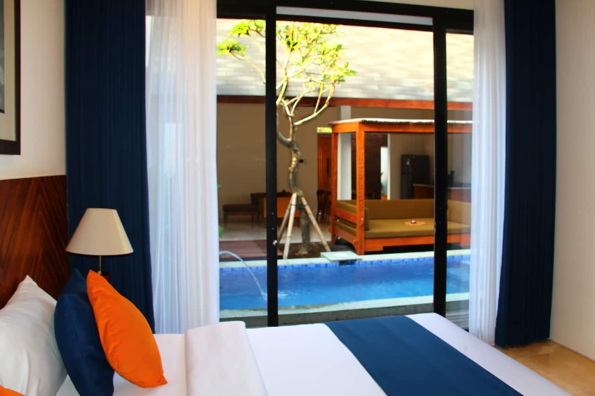 A hotel room with a bed, a lamp, and a view of a pool and outdoor seating area.