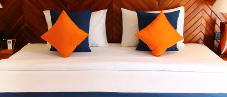 Una cama con ropa de cama blanca y azul, dos almohadas naranjas y un cabecero de madera con diseño de espiga.