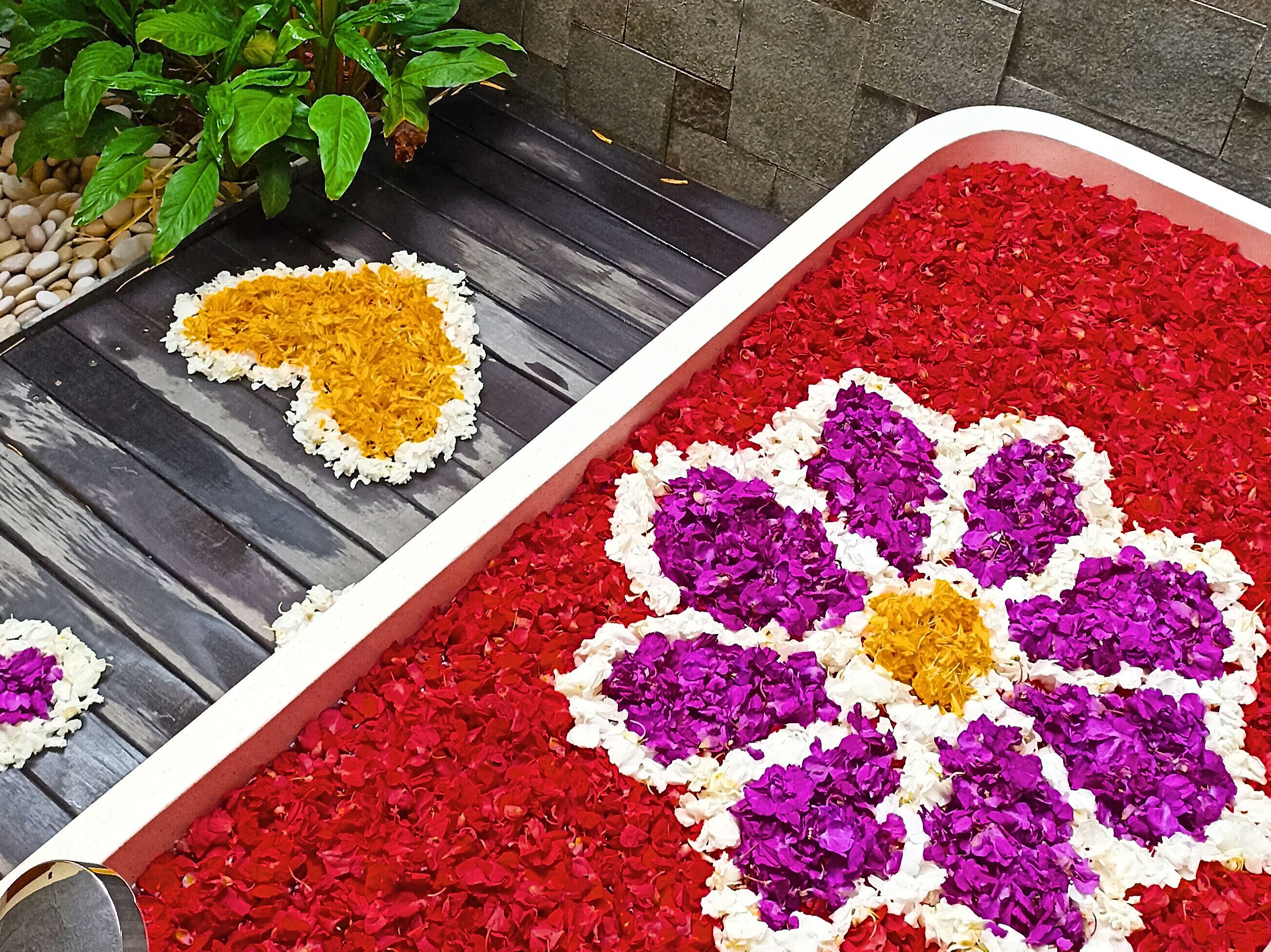 Un récipient rectangulaire rempli de pétales de fleurs rouges et violettes, disposées en forme de cœur.