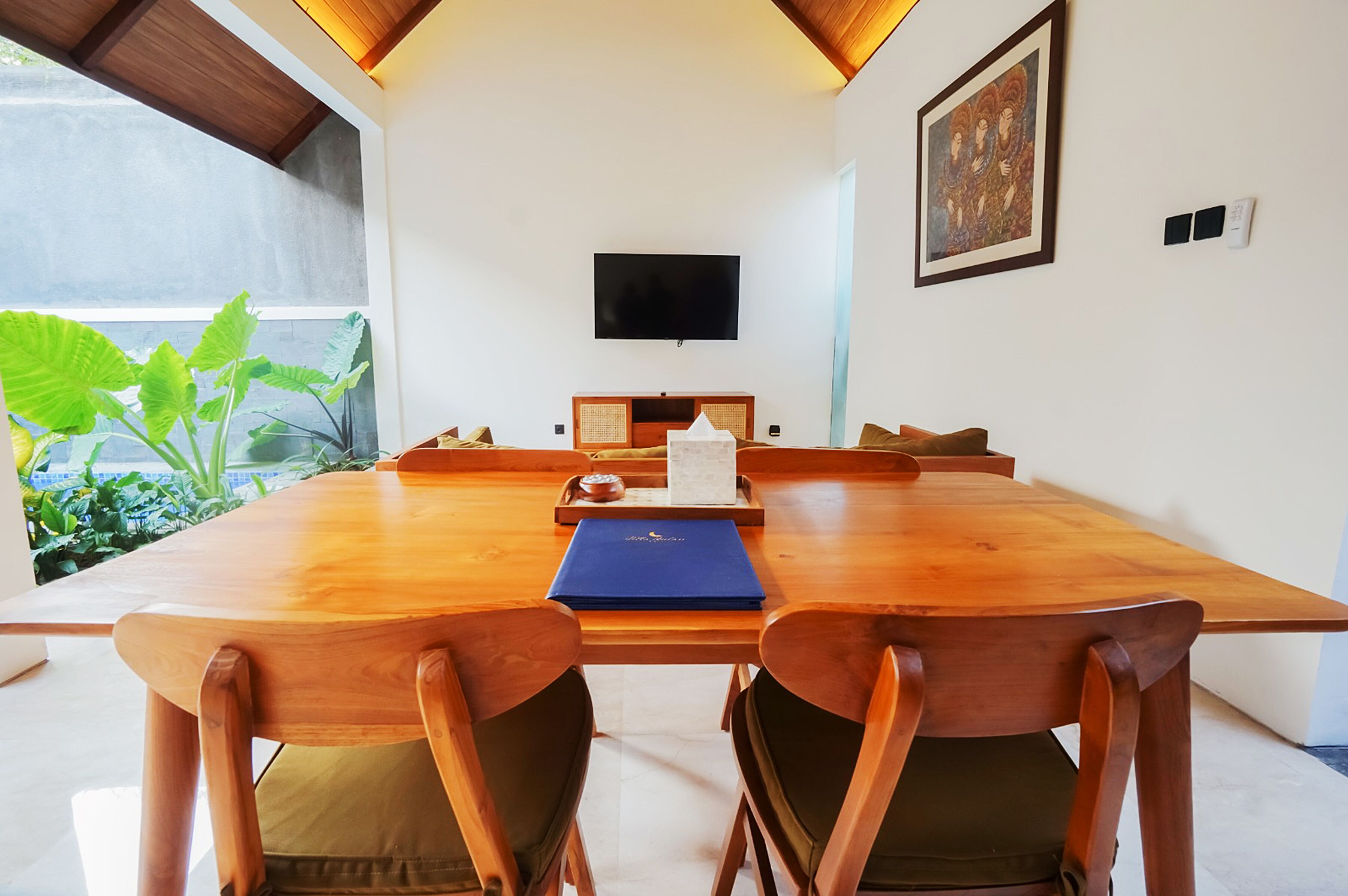 A wooden dining table with chairs, a flat-screen TV mounted on the wall, and a framed painting above it.