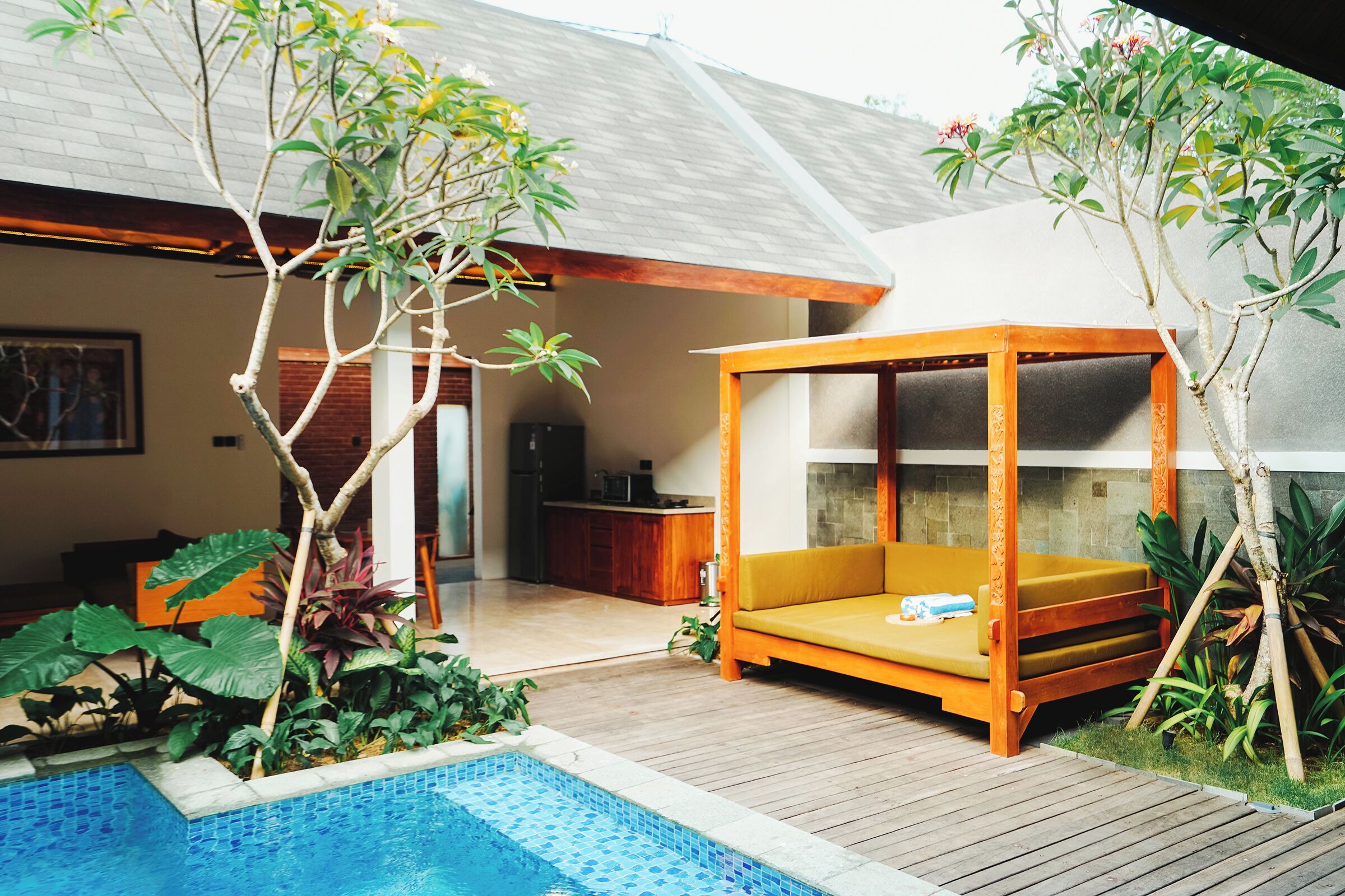A modern outdoor living area with a wooden deck, a small pool, and a wooden canopy bed.