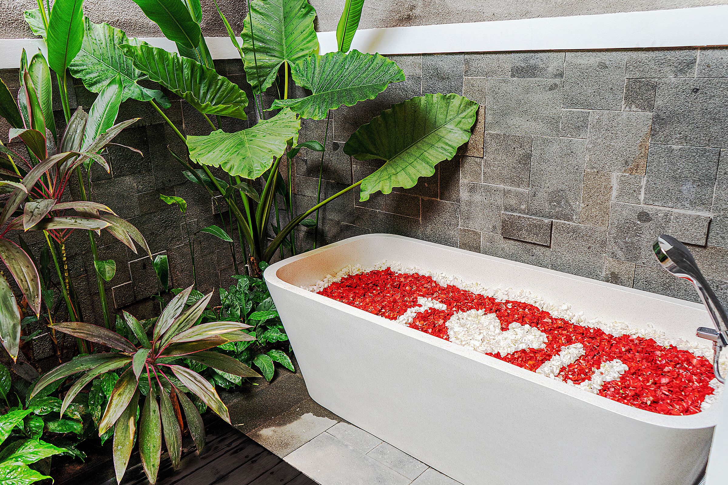 A bathtub filled with red and white pebbles, surrounded by large green plants.