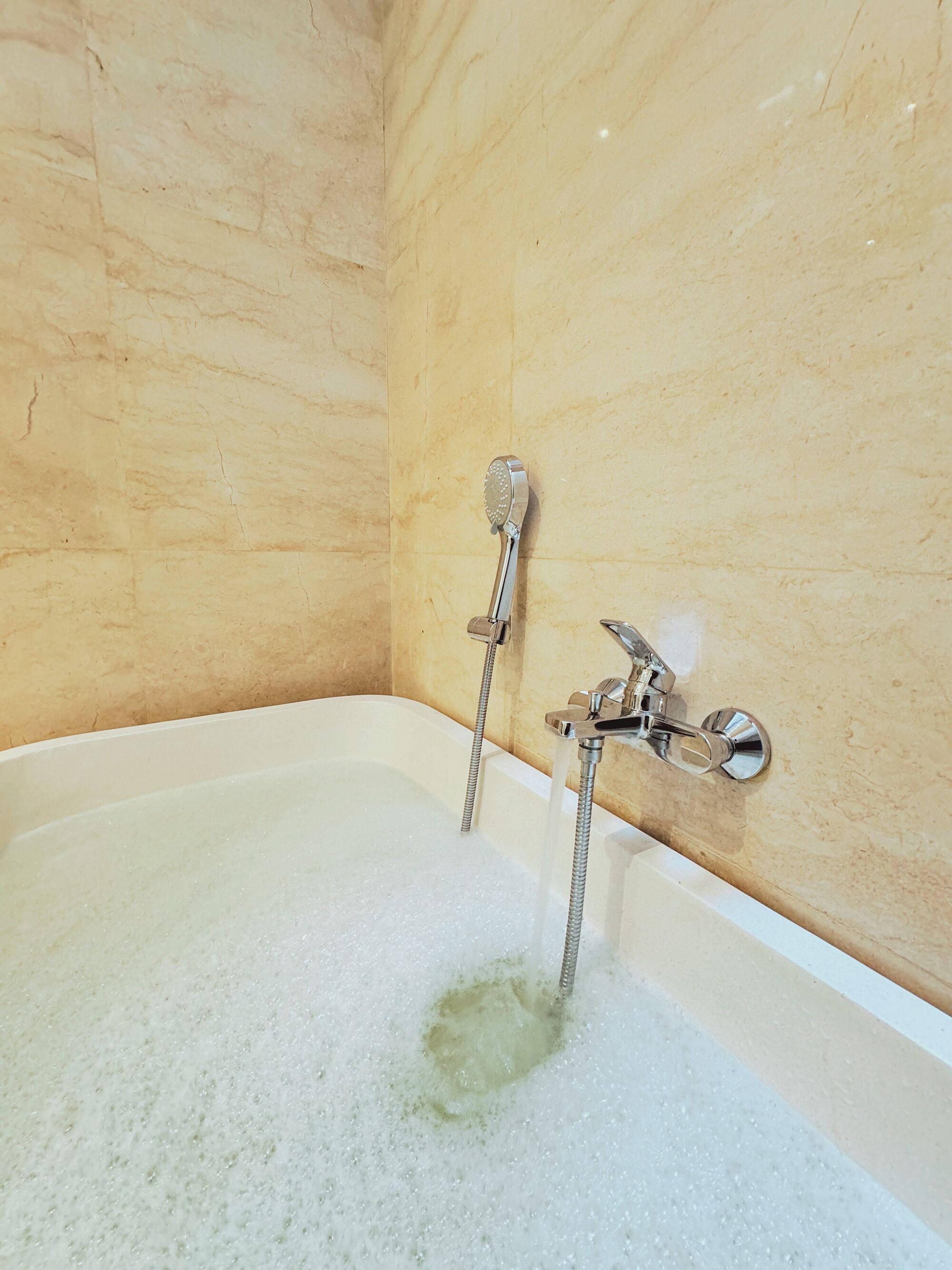 A bathtub with running water and bubbles, a handheld showerhead, and a wall-mounted faucet.