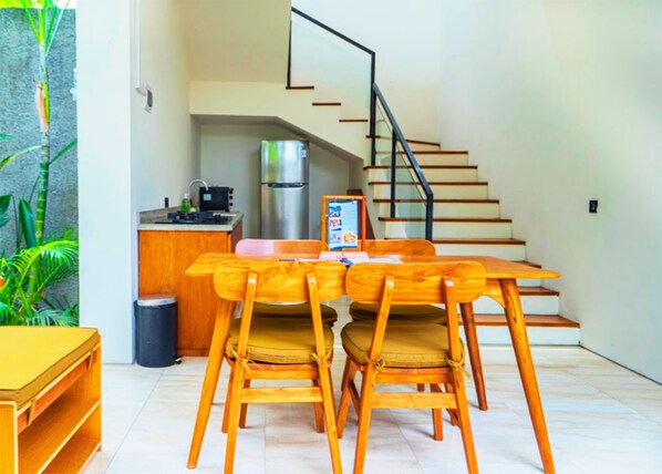A modern kitchen with a dining area, a staircase, and a trash bin.