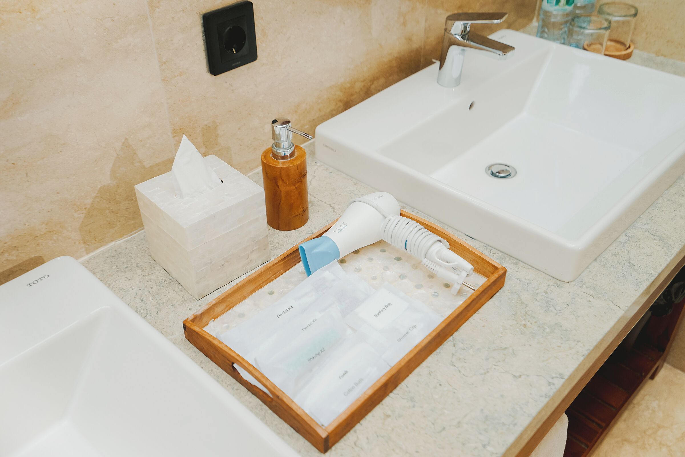 A bathroom with two sinks, a wooden tray with toiletries, a bottle of hand sanitizer, and a box of tissues.