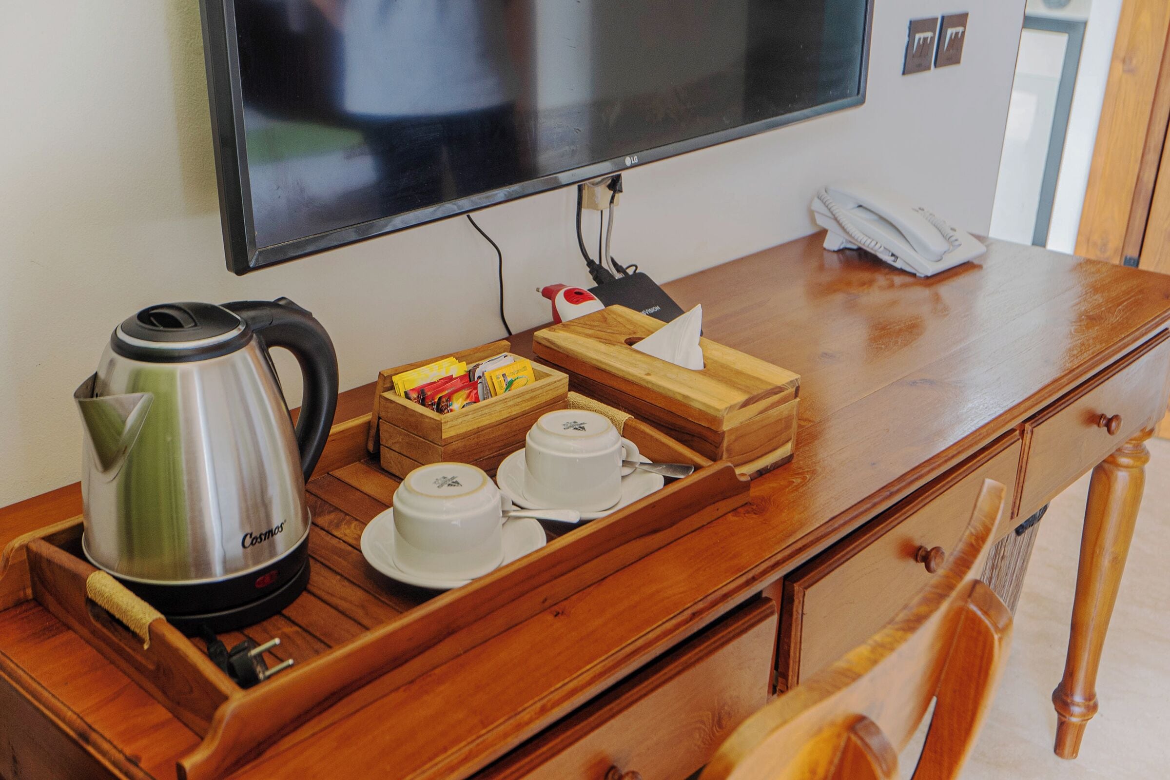 A wooden desk with a kettle, teacups, and a box of tissues.