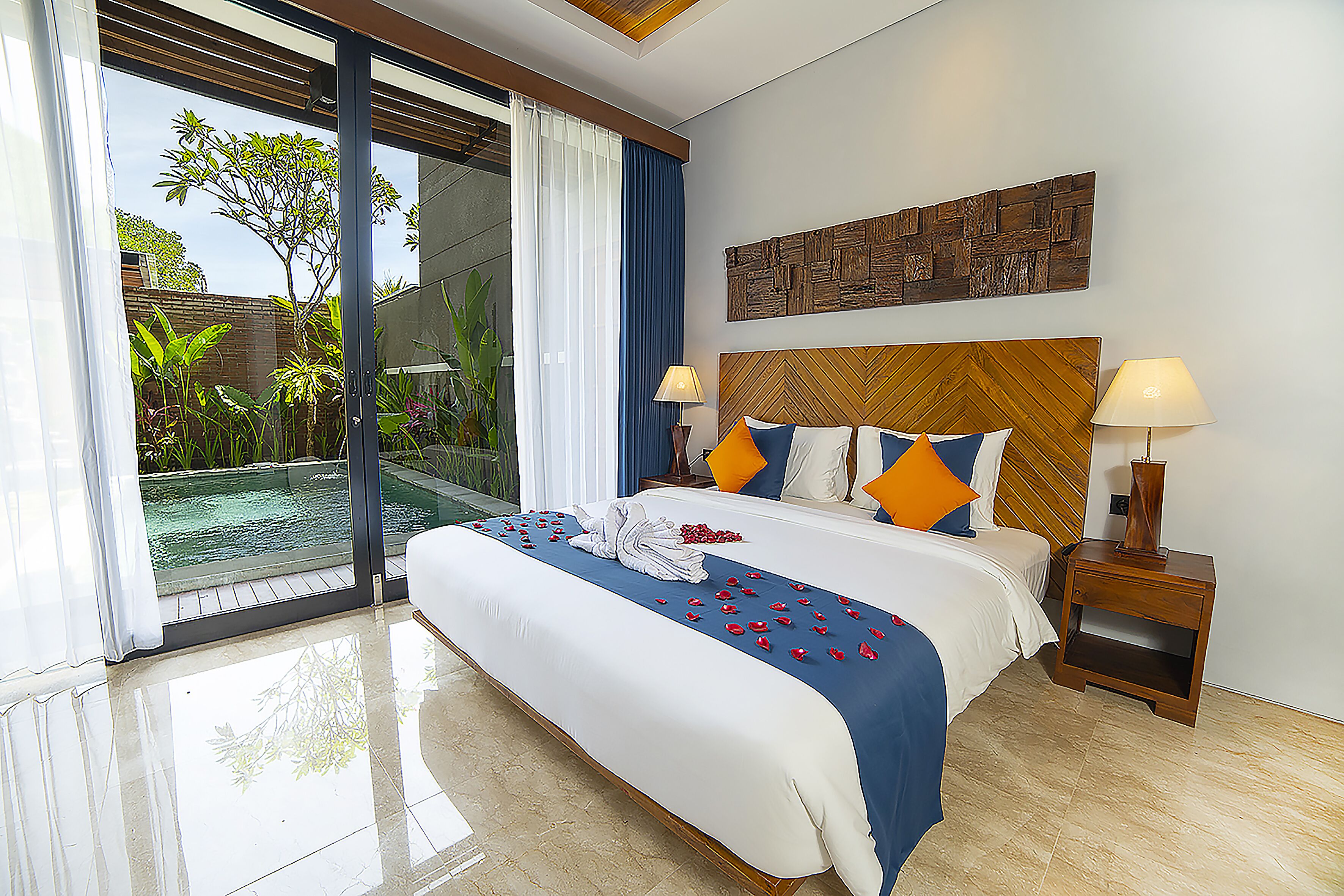 Habitación de hotel con una cama grande, dos lámparas de noche, cabecera de madera y vistas a una piscina.