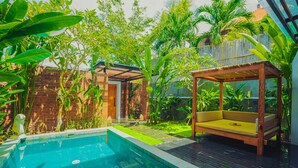 A pool area with a wooden deck, a small garden, and a wooden bench. - Villa Bulan Bali (Jimbaran)
