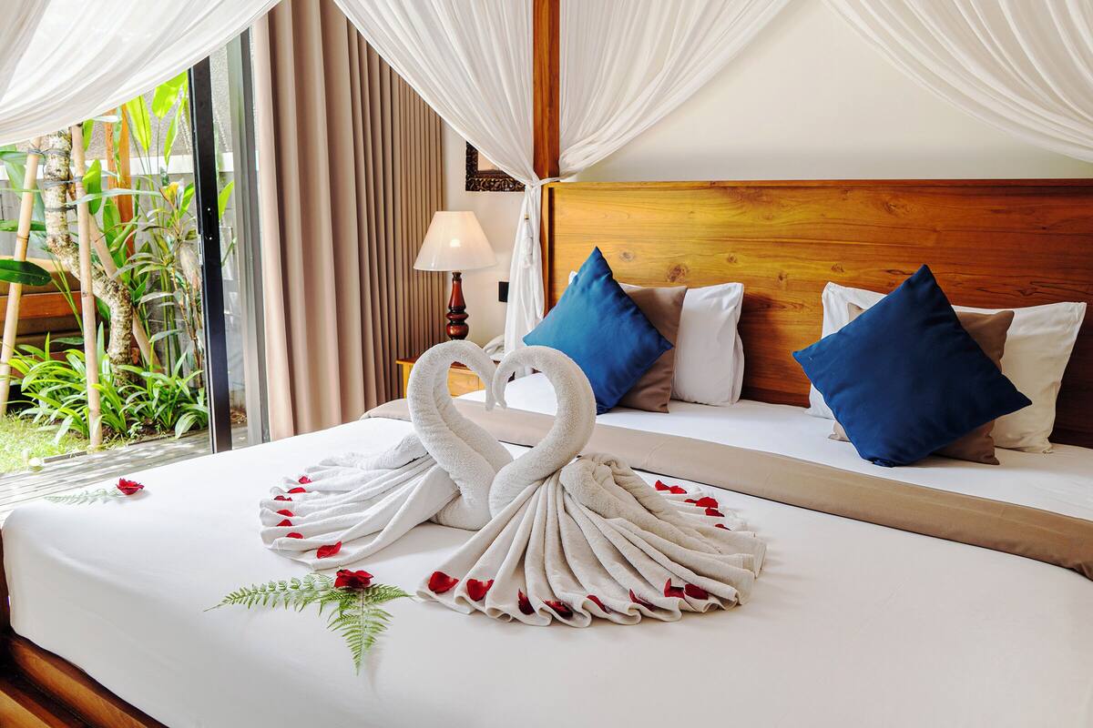 A hotel room with a large bed, a wooden headboard, and a view of greenery outside.