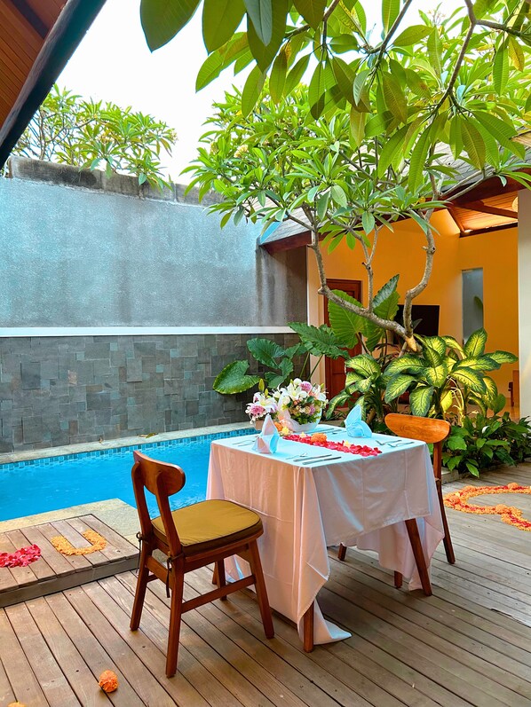 Una terraza de madera con una mesa dispuesta para dos, una silla y una pequeña piscina.