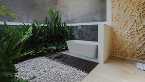 A modern bathroom with a stone wall, a bathtub, and a pebble pathway. - Villa Bulan Bali (Jimbaran)