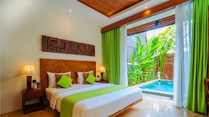 A hotel room with a large bed, wooden headboard, green curtains, and a view of a swimming pool. - Villa Bulan Bali (Jimbaran)
